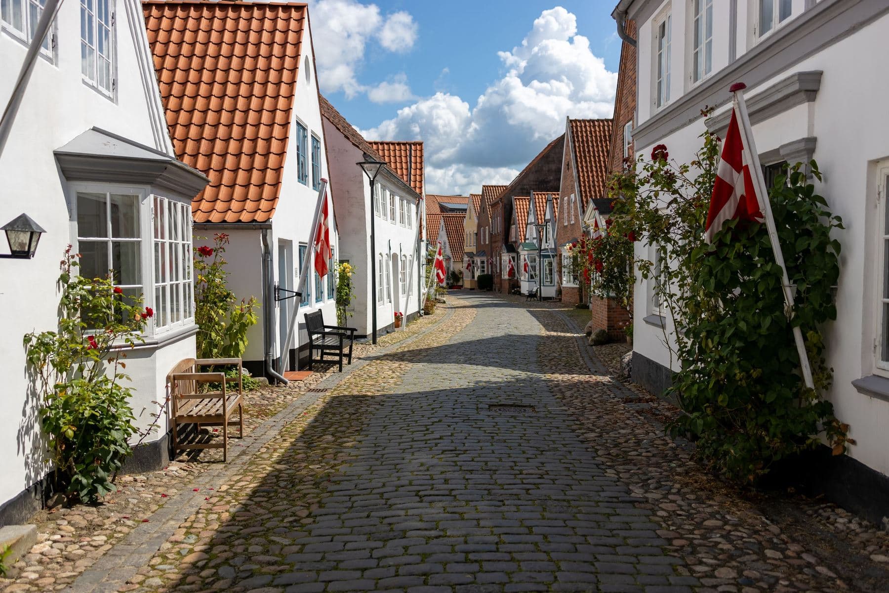 Kopfsteinpflaster-Gasse mit weissen Häusern und Dannebrog-Fahnen in der Altstadt von Tønder