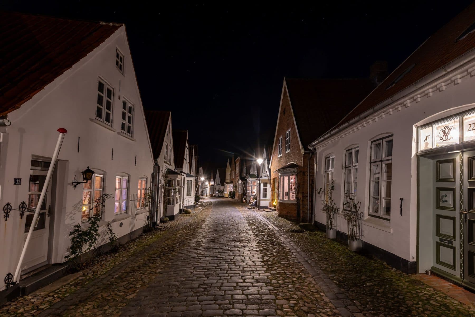 Oplyst brostensgade med hvide huse i Tønder om natten