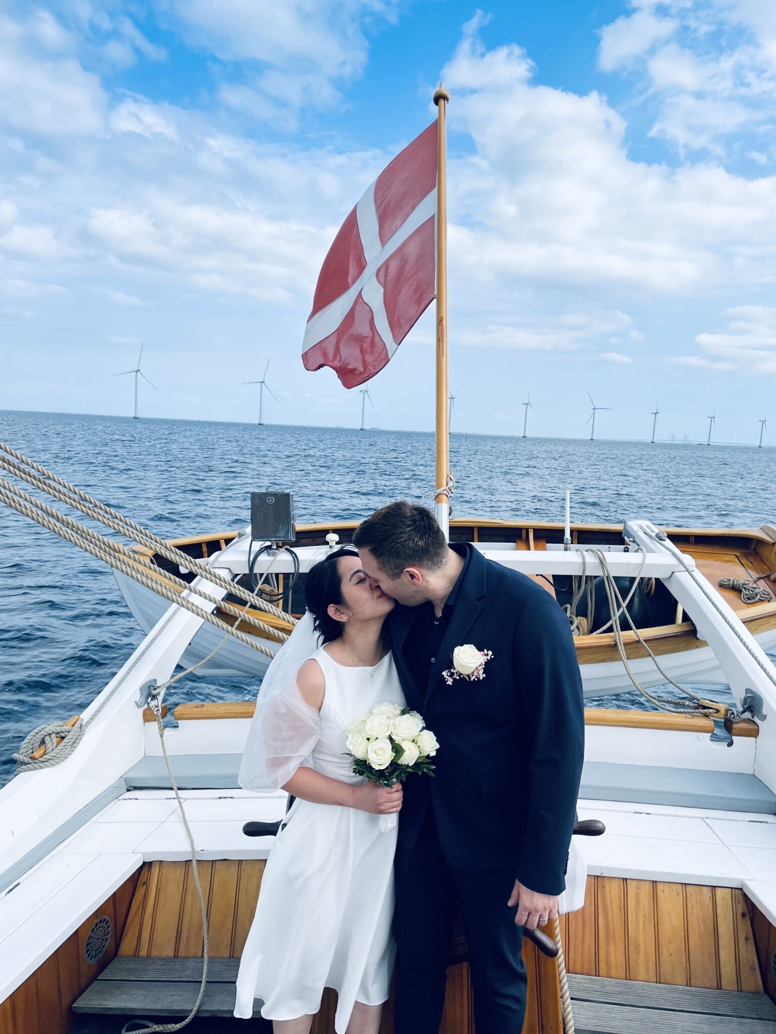 Alexander und Thi Yen küssen sich auf einem traditionellen dänischen Boot mit dänischer Flagge.