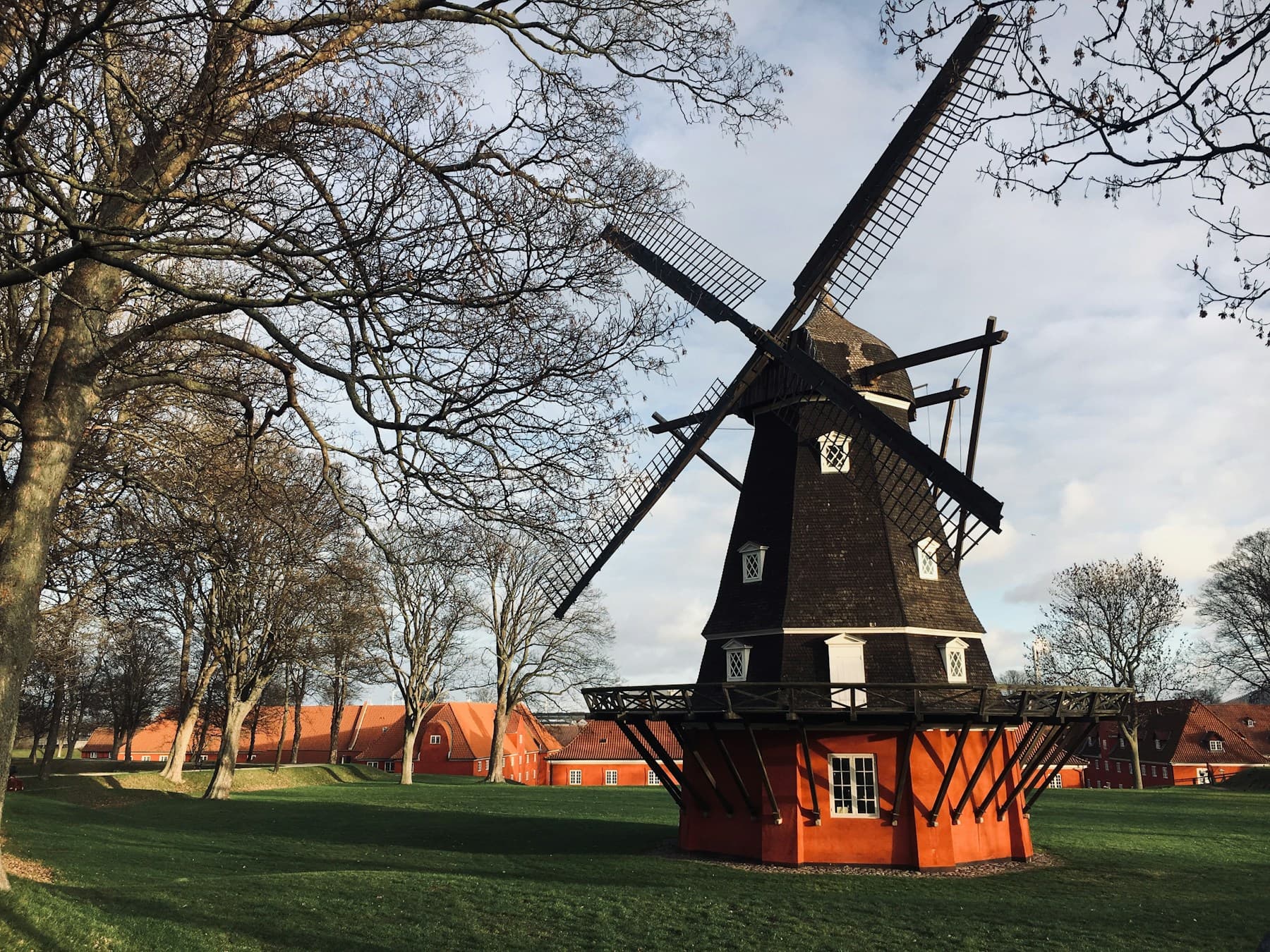 Historische Windmühle zwischen Bäumen, dahinter rote Häuser